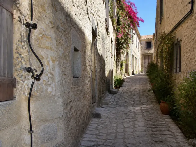 Ruelle pavée d’un village médiéval provençal, façades en pierre et câbles anciens en façade